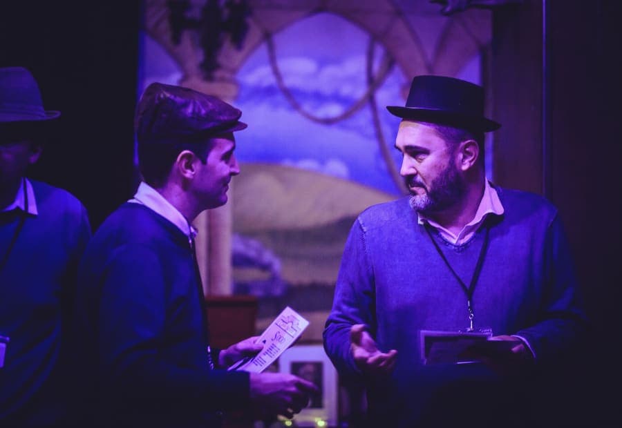 Colleagues in 1920s hats comparing their character files at a corporate murder mystery in Barcelona